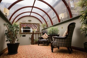 A reception area with a high arched ceiling, a mirror, a reception desk, two chairs, and potted plants. - Grand Hotel Tralee (Tralee)