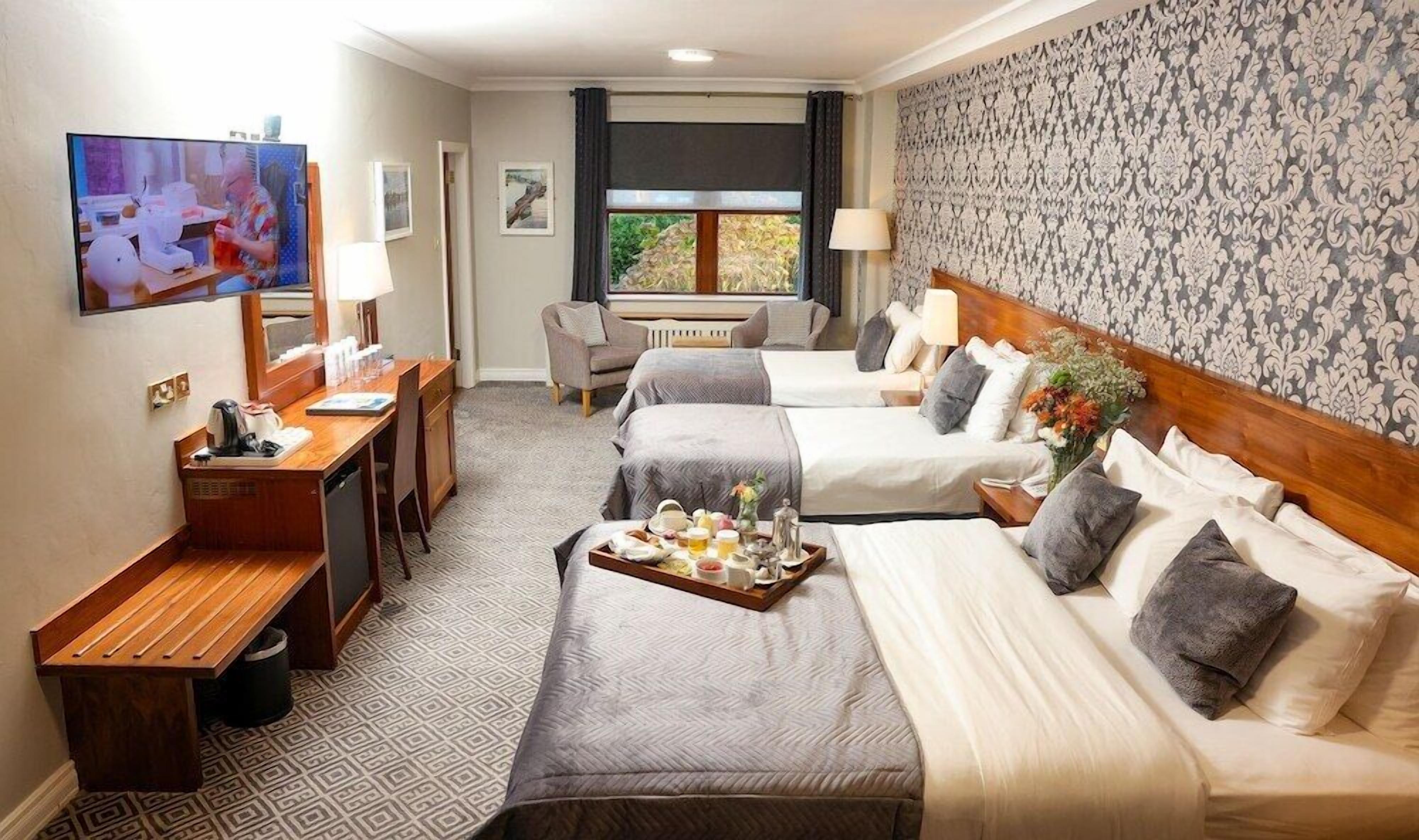 A hotel room with two beds, a desk, a TV, and a window with a view.