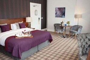 Habitación de hotel con cama, escritorio, dos sillas, lámpara y un cuadro en la pared.