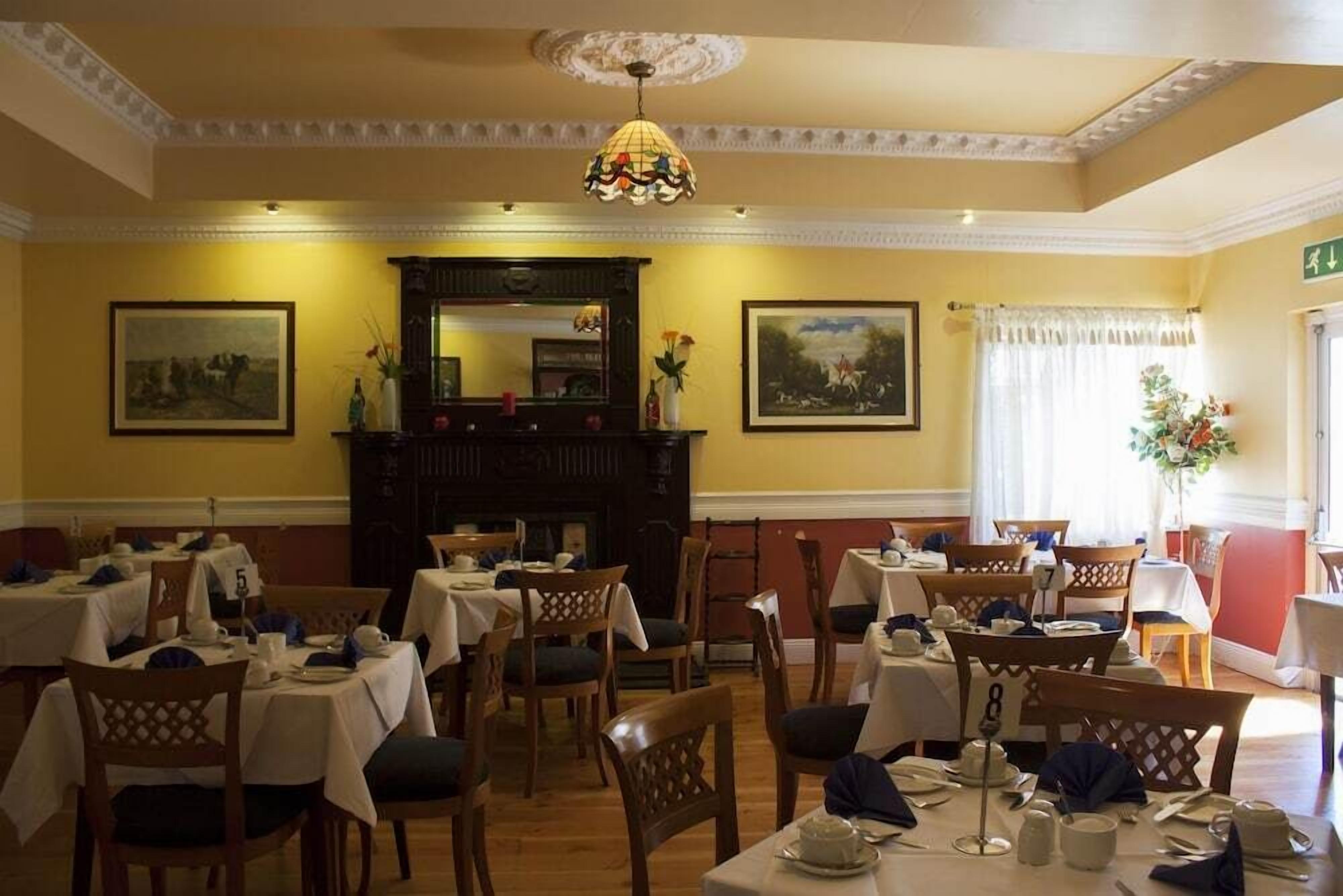 A dining area with tables set for service, wooden chairs, a chandelier, and framed artwork on the walls.