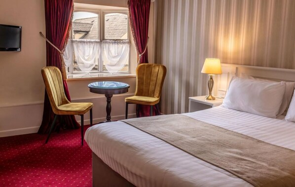 A hotel room with a bed, two chairs, a small table, a lamp, and a TV. - Kees (Stranorlar)