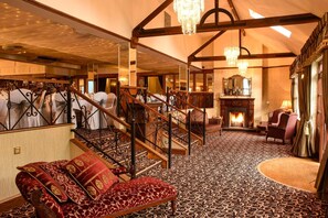 A grand room with a patterned carpet, a wooden staircase, and a fireplace.
