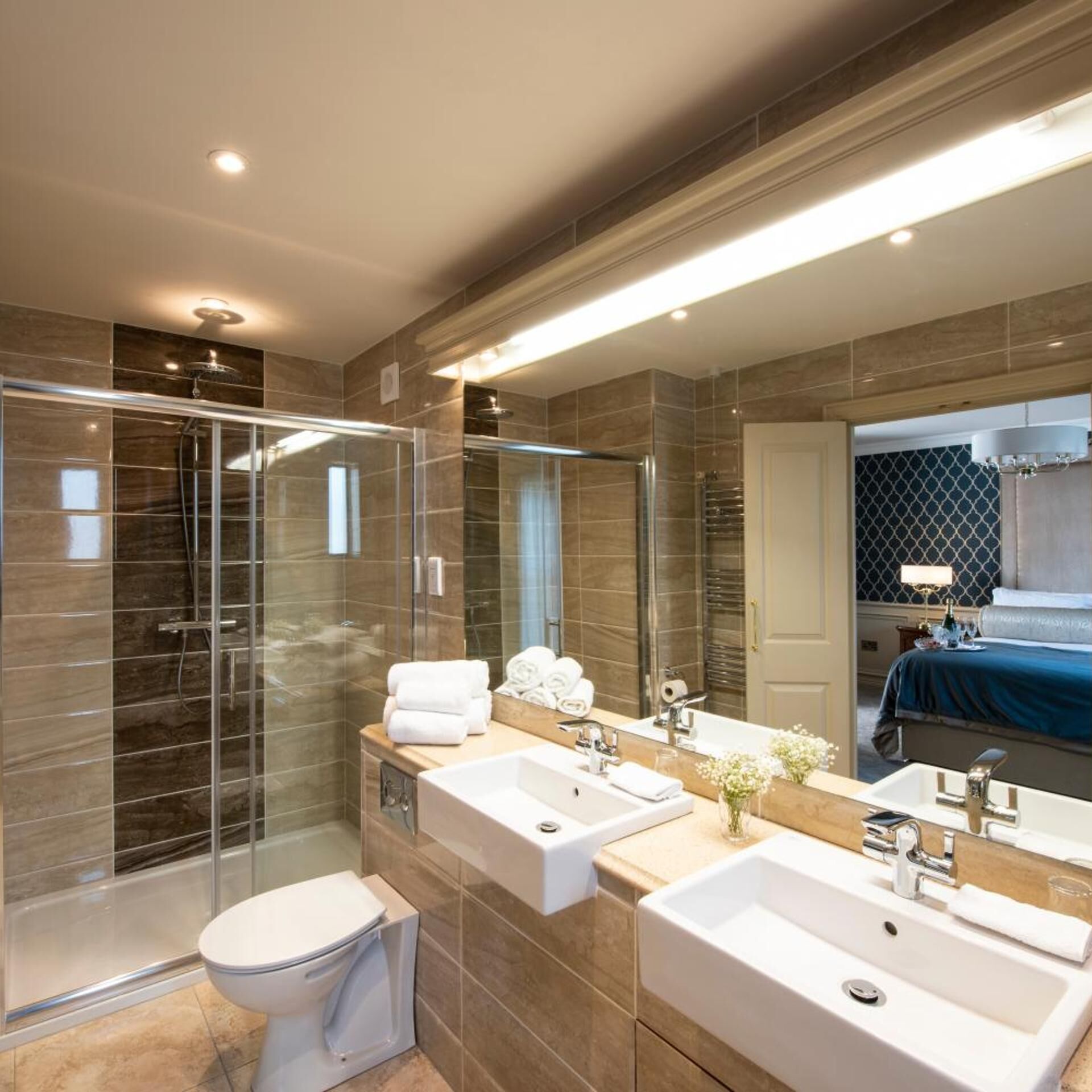 Une salle de bain moderne dotée d’une douche à parois de verre, de toilettes et d’un meuble-lavabo avec deux vasques.