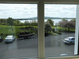 A view of a parking area with a boat, cars, and a golf course in the background.