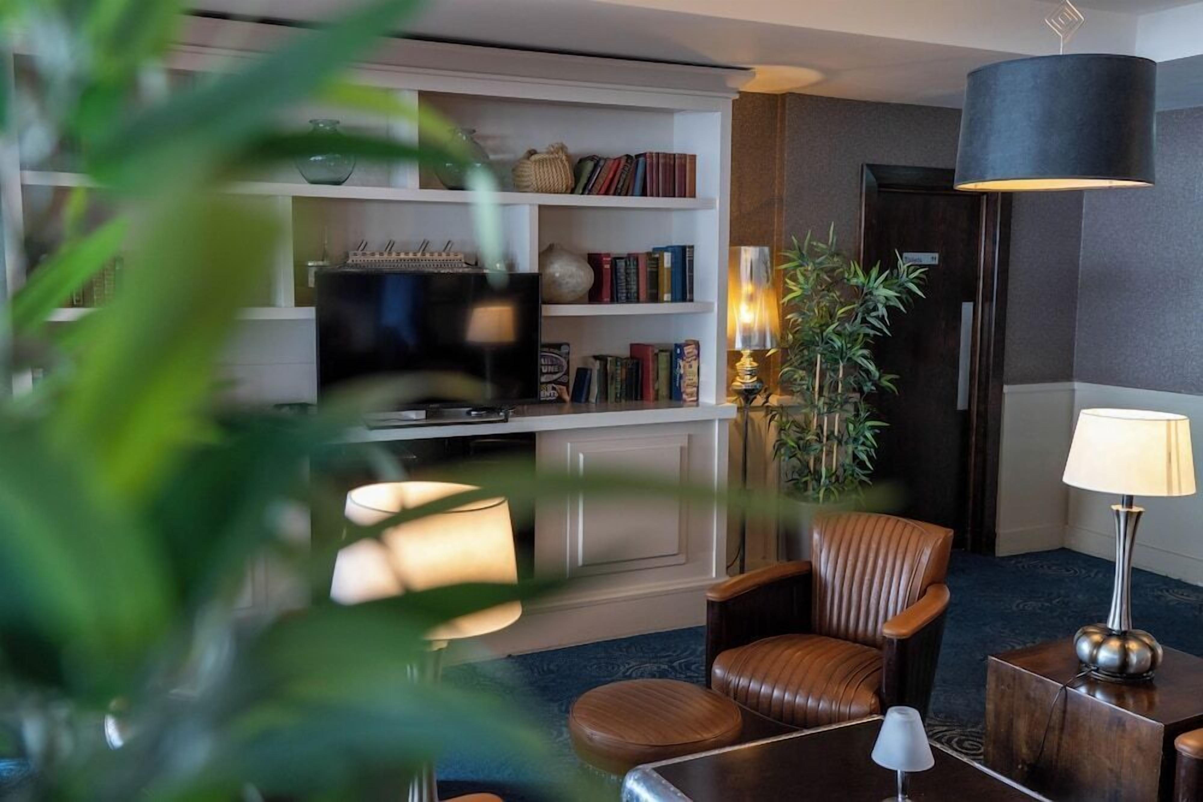 A modern living room with a television, bookshelves, a leather armchair, a side table, and a lamp.