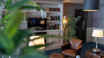 A modern living room with a television, bookshelves, a leather armchair, a side table, and a lamp.