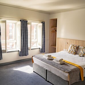 A hotel room with a bed, a wooden wardrobe, and a window with curtains.