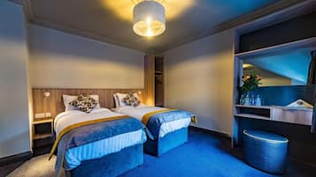 Habitación de hotel con dos camas, un espejo grande, una mesita de noche y una alfombra azul.