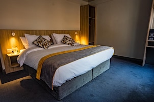 A modern hotel room with a large bed, a wooden headboard, and a built-in wardrobe.