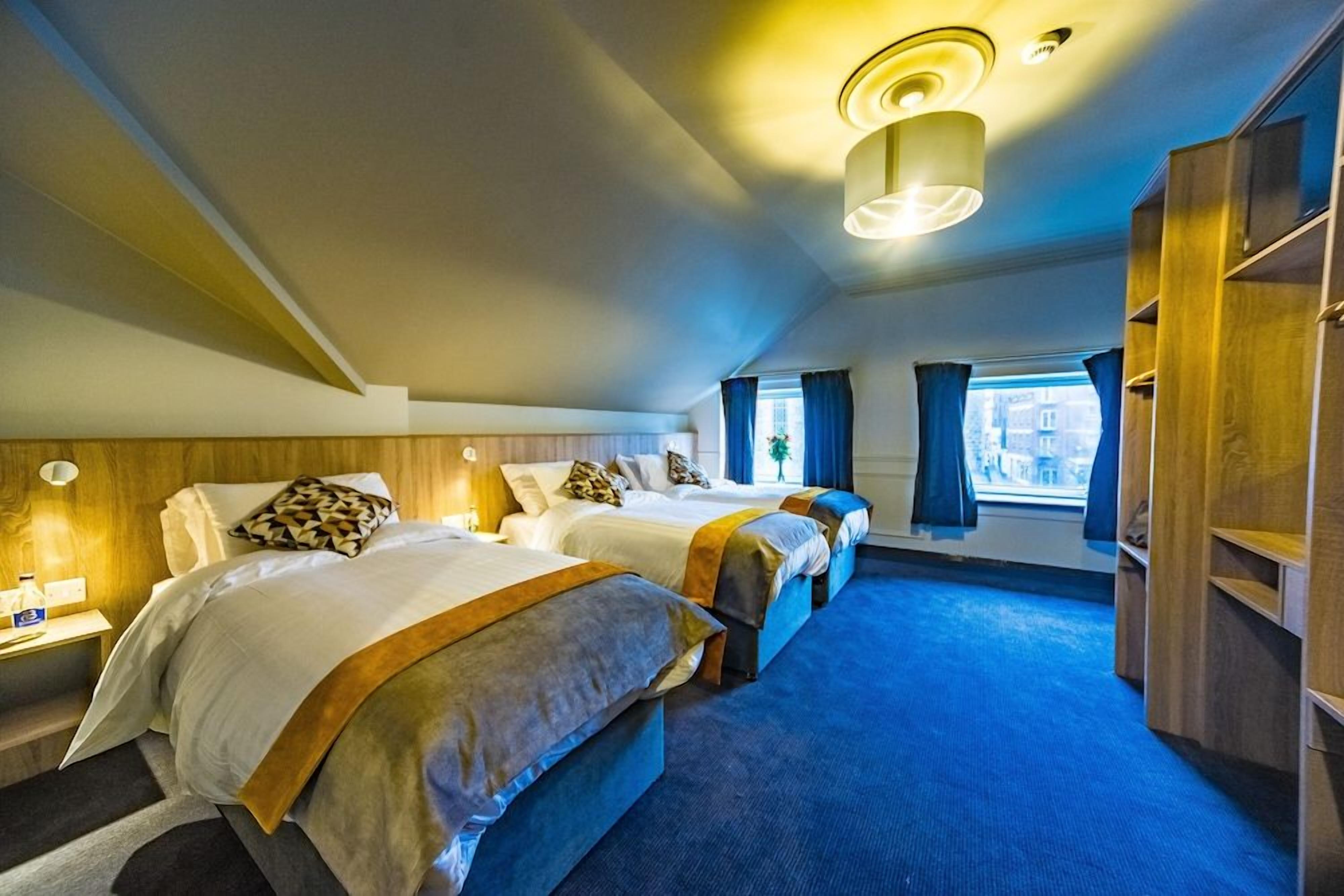Habitación de hotel con tres camas, un ventanal grande y una alfombra azul.