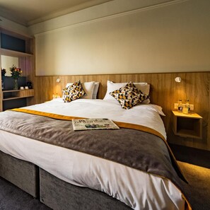 A hotel room with a large bed, a bedside table with a lamp, a nightstand, and a mirror above the bed.