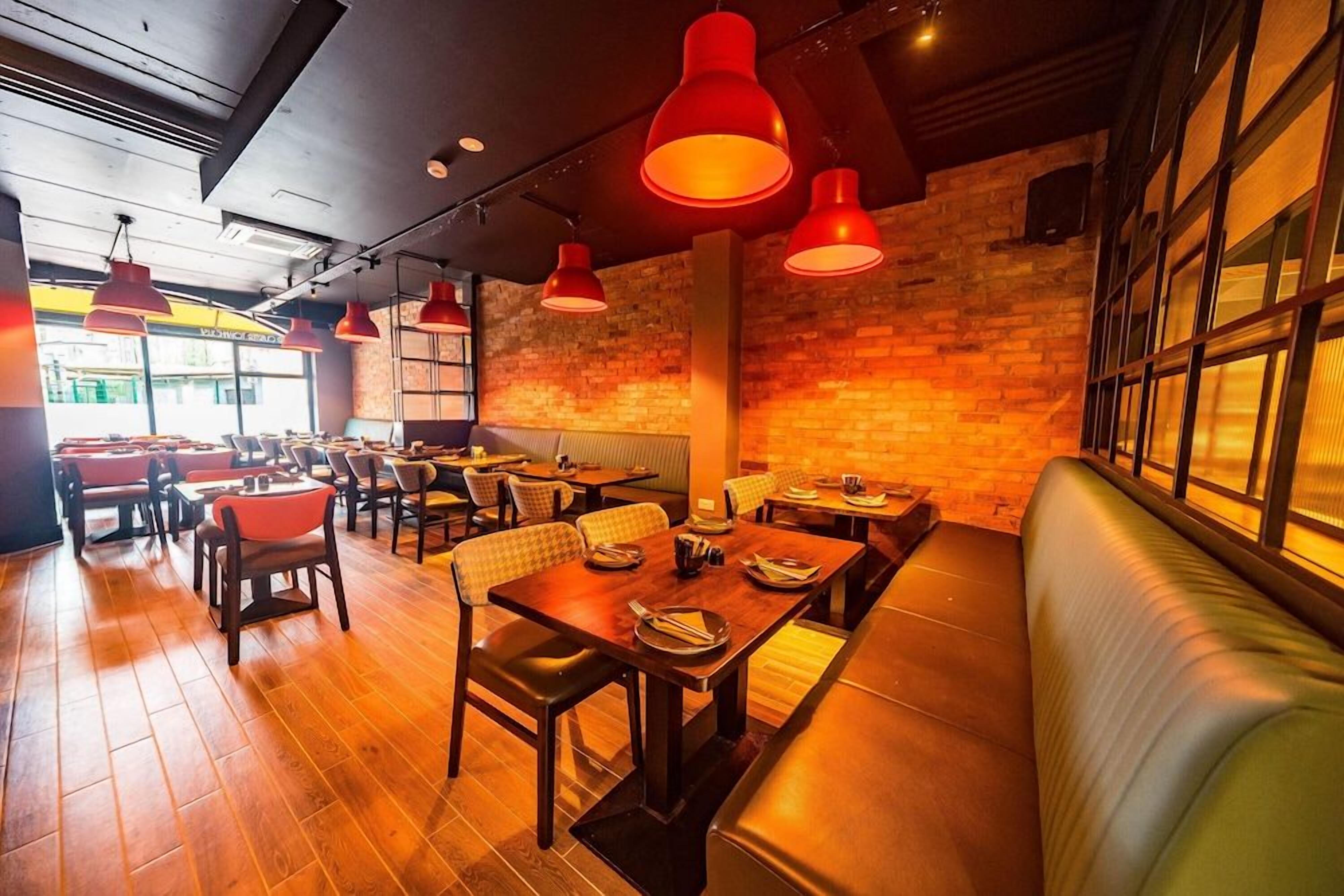 Interior de restaurante con suelo de madera, iluminación colgante roja, paredes de ladrillo y una combinación de asientos tipo cabina y mesas.