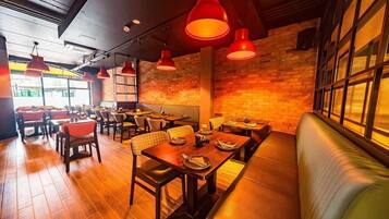 Interior de restaurante con suelo de madera, iluminación colgante roja, paredes de ladrillo y una combinación de asientos tipo cabina y mesas.