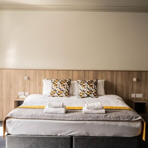 A neatly made bed with two pillows, a bedside table, and a wall-mounted light.