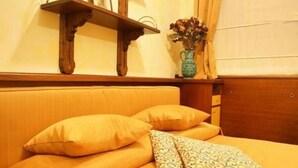 A bed with yellow bedding and pillows, a wooden headboard, a small wooden shelf with a vase of flowers, and a wooden cabinet. - Residence Tynska (Prague)