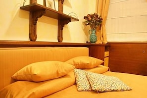 A bed with yellow bedding and pillows, a wooden headboard, a small wooden shelf with a vase of flowers, and a wooden cabinet. - Residence Tynska (Prague)