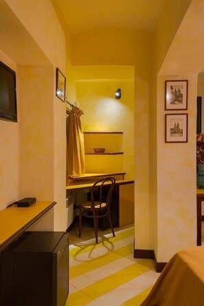 Habitación de hotel compacta con un escritorio pequeño, una silla, una cama y televisión en la pared.