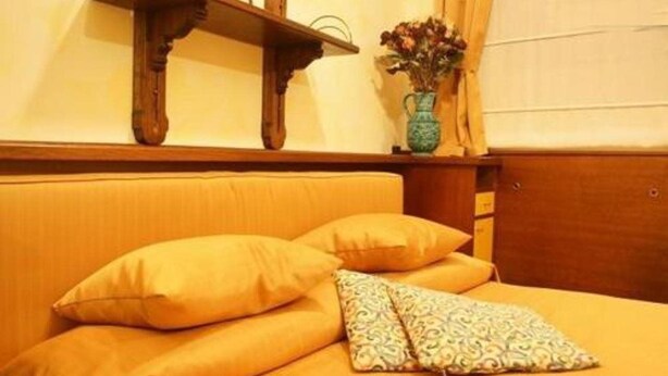A room with a bed, a wooden headboard, a small wooden shelf, and a vase with flowers. - Residence Tynska (Prague)