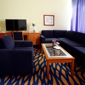 A living room with a sofa, armchair, and a coffee table with a vase and glass. - Hotel Central (Plzen)
