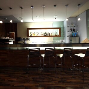 A bar area with a wooden bar counter, multiple hanging lights, and bar stools. - Hotel Central (Plzen)