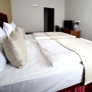 A hotel room with a bed, pillows, a desk with a chair, a television, and a vase with flowers. - Hotel Central (Plzen)