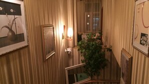 A narrow hallway with striped wallpaper, a framed picture on the left, a wall-mounted light fixture, and a potted plant. - Chipilakoff (Burgas)