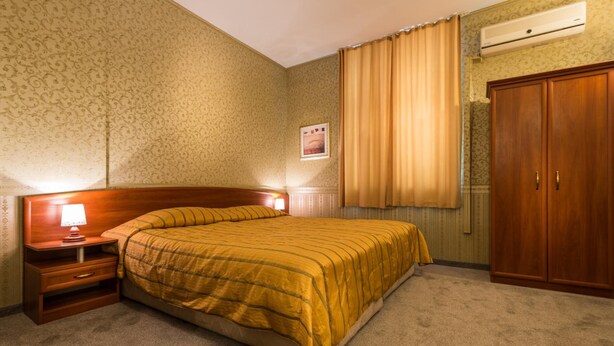 Une chambre d’hôtel comprenant un lit, une table de chevet, une lampe, une armoire et une fenêtre avec des rideaux.