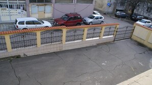 Un espace de stationnement délimité par une clôture jaune, avec une voiture rouge garée au centre.
