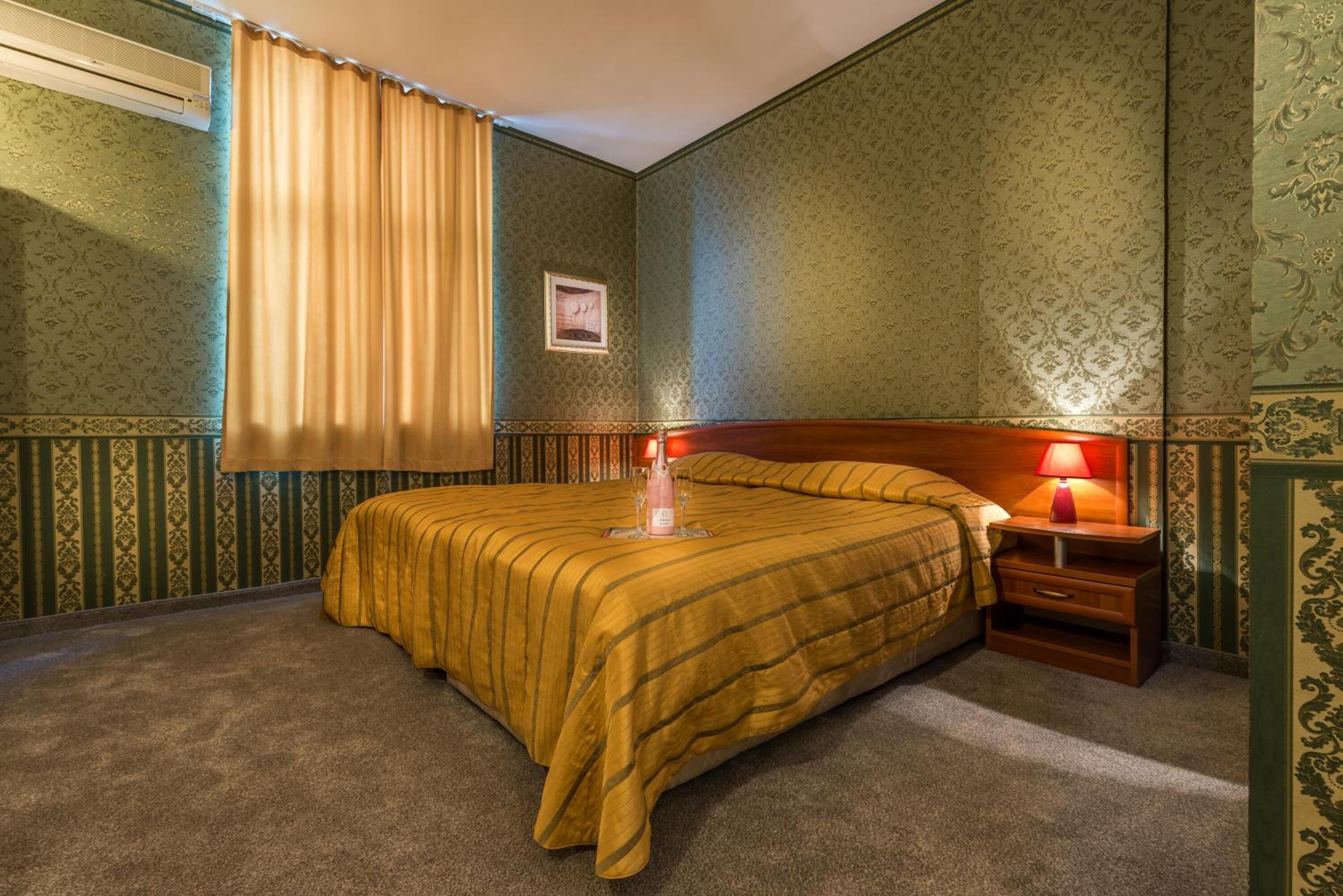 A hotel room with a bed, a nightstand, a lamp, and a picture on the wall.