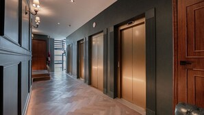 A hallway with wooden flooring, a black leather bench, and a set of elevators. - The Green Escape Suite (Mexico City)
