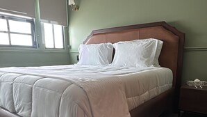 A bedroom with a large bed, a nightstand, a window with blinds, and a green wall. - The Green Escape Suite (Mexico City)