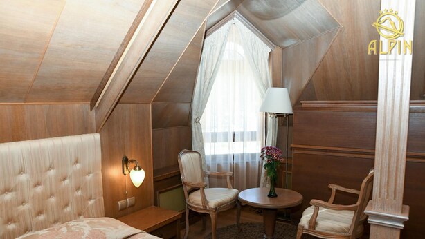 A cozy hotel room with a large bed, a small round table, two chairs, and a window with sheer curtains. - Alpin (Samokov)