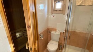 A bathroom with a toilet, a shower, and a wooden door leading to another room. - Alpin (Samokov)