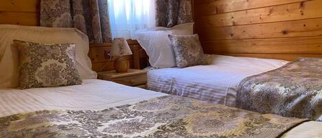A wooden cabin room with two beds, a nightstand, and a window with curtains.