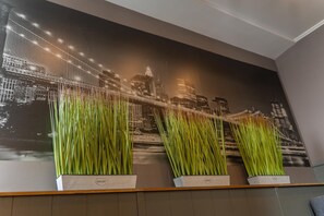 A wall with a cityscape mural, three potted plants, and a wooden panel. - City Hotel (Veliko Tarnovo)