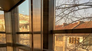 A view from inside a building with large windows, revealing a street scene with buildings and bare trees. - City Hotel (Veliko Tarnovo)