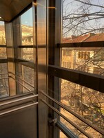 A view from inside a building with large windows, revealing a street scene with buildings and bare trees.