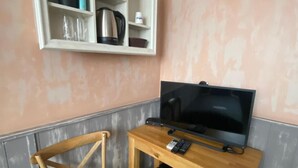 A small room with a television, a wooden chair, a shelf with a plant, and a kettle. - City Hotel (Veliko Tarnovo)