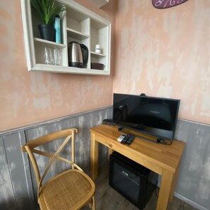 A small room with a television, a wooden chair, a shelf with a plant, and a kettle. - City Hotel (Veliko Tarnovo)