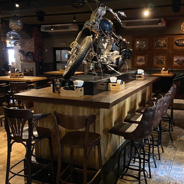 Zona de bar con mostrador central, taburetes y una decoración con una motocicleta.