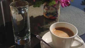 Une table avec une tasse de café, un verre d’eau et un vase de fleurs.