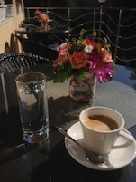 Uma mesa com uma xícara de café, um copo de água e um vaso de flores.