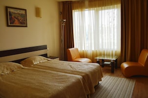 Quarto de hotel com duas camas, uma cadeira, uma mesinha e um quadro na parede.