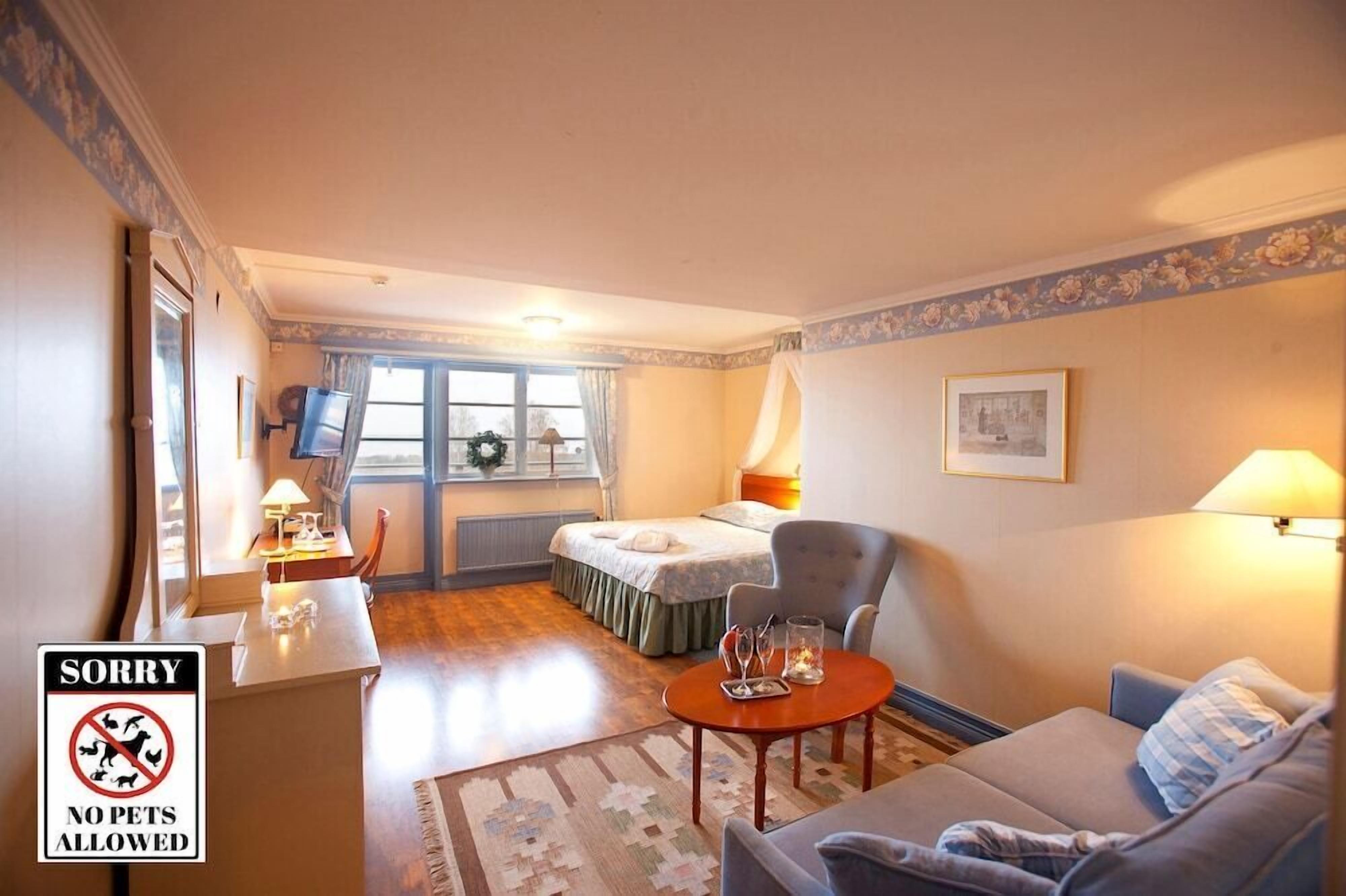 Ett hotellrum med en säng, en soffa, ett skrivbord och en stol. På skrivbordet finns en skylt med texten ”Husdjur ej tillåtna”.