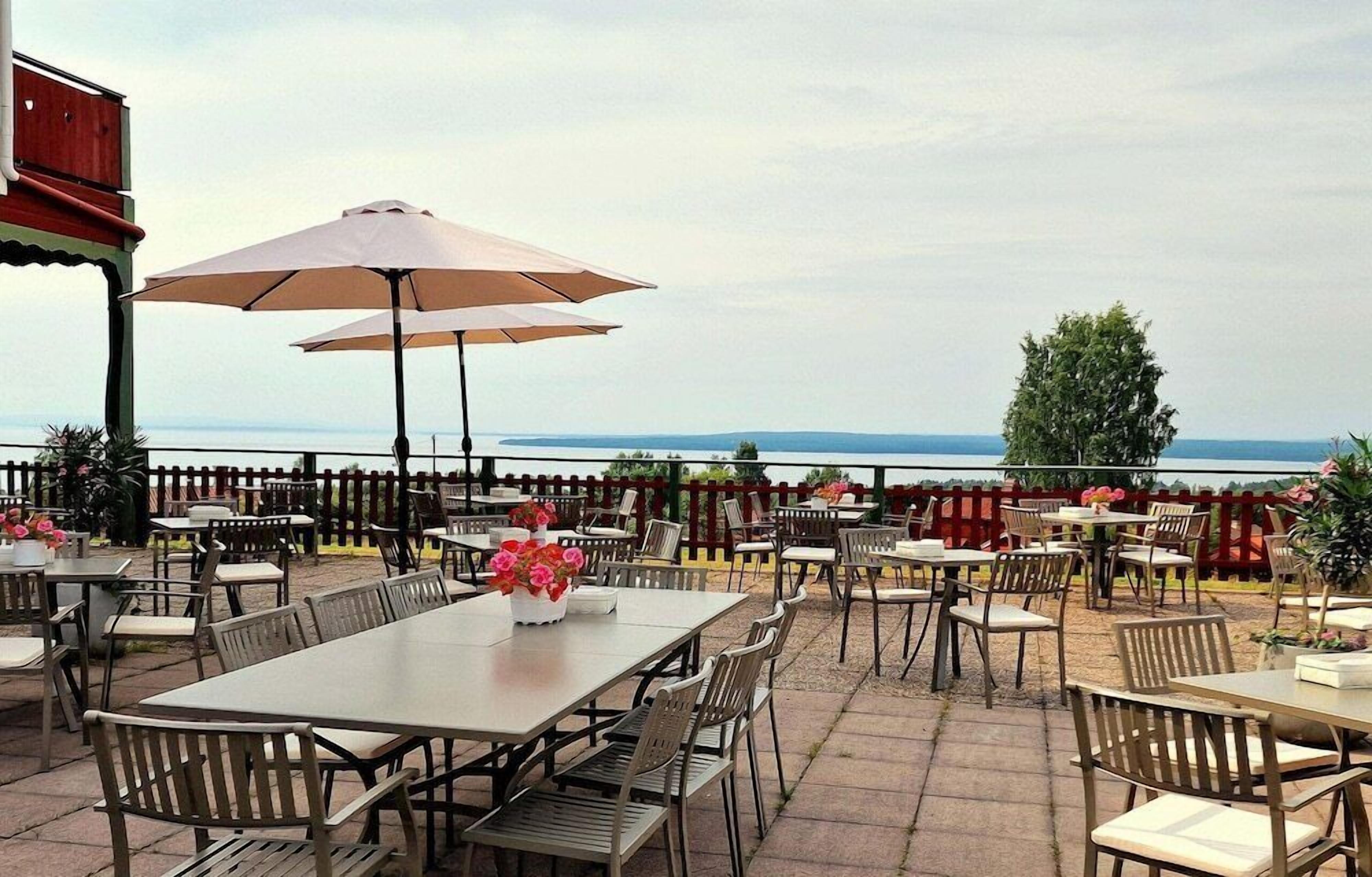 An outdoor patio area with tables and chairs, a wooden fence, and a view of the sea.