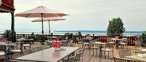 An outdoor patio area with tables and chairs, a wooden fence, and a view of the sea.