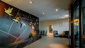 A modern reception area with a dark wooden reception desk, a sign reading "Mikolajki Resort Hotel & Spa", and a seating area with chairs and a small table. - Hotel Mikolajki Resort By Desilva (Mikolajki)