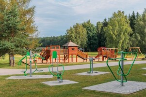 Un parque infantil con equipos de ejercicio, una casita de madera y un tobogán.