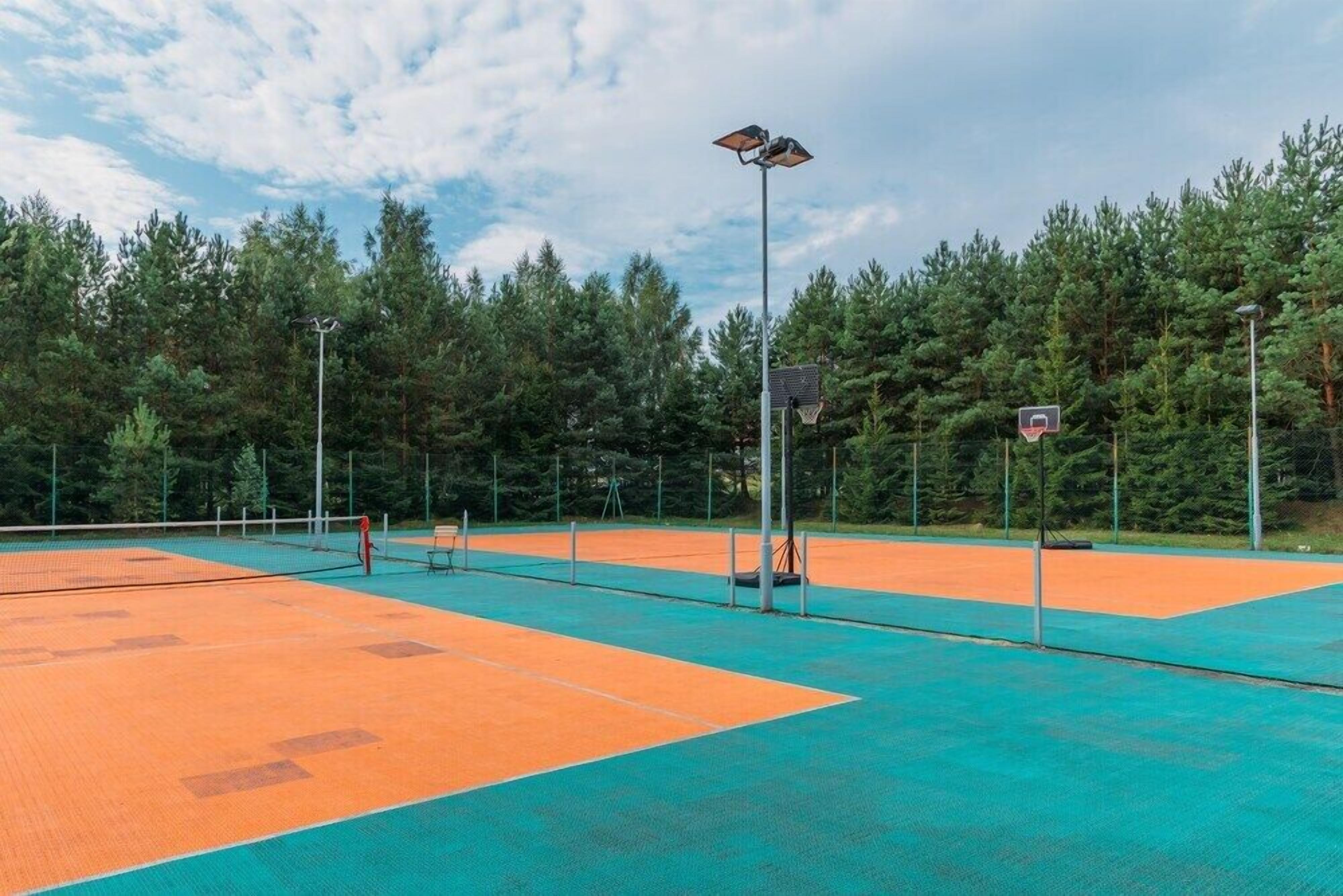 An outdoor tennis court with multiple courts, surrounded by trees.