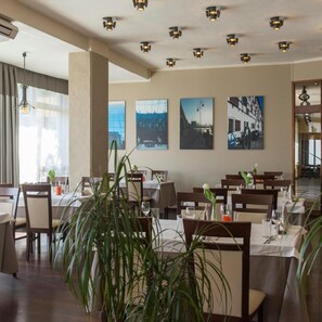 Un restaurante con mesas dispuestas para comer, obras de arte en las paredes y un techo con iluminación empotrada.